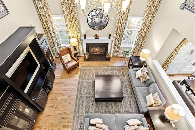 living area with wood finished floors, plenty of natural light, a fireplace, and a towering ceiling