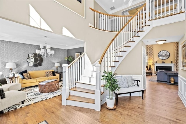 staircase with wallpapered walls, an accent wall, crown molding, a chandelier, and wood finished floors