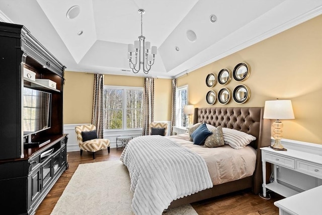 bedroom featuring an inviting chandelier, a raised ceiling, wood finished floors, and a wainscoted wall