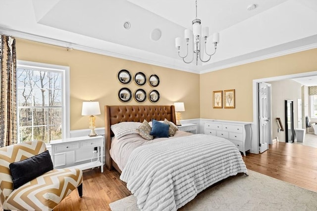 bedroom with a tray ceiling, multiple windows, wood finished floors, and ornamental molding