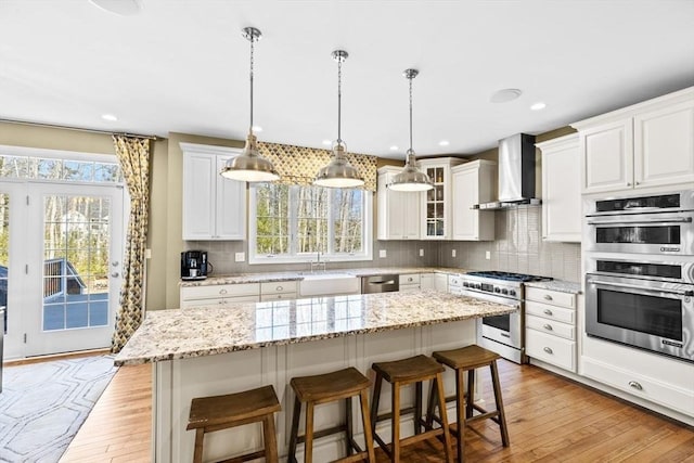 kitchen featuring a breakfast bar area, light wood finished floors, stainless steel appliances, wall chimney exhaust hood, and backsplash