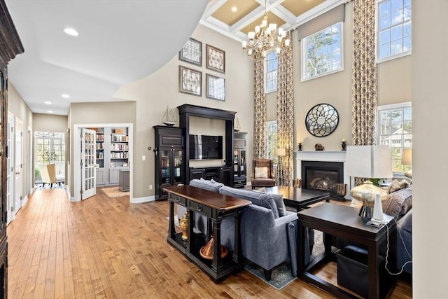 living room featuring beamed ceiling, coffered ceiling, a glass covered fireplace, light wood-style floors, and baseboards