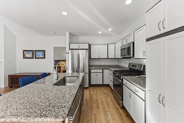 kitchen featuring sink, an island with sink, light stone counters, and stainless steel appliances