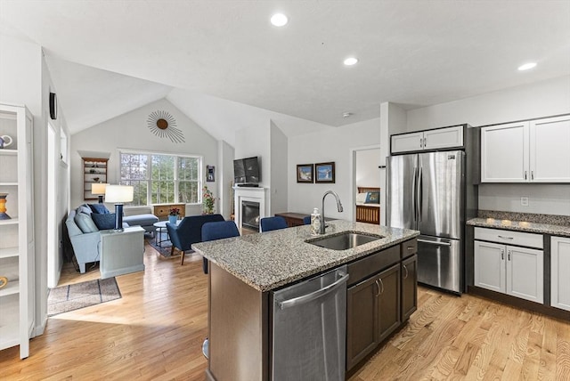 kitchen featuring sink, a kitchen island with sink, appliances with stainless steel finishes, white cabinets, and light stone counters