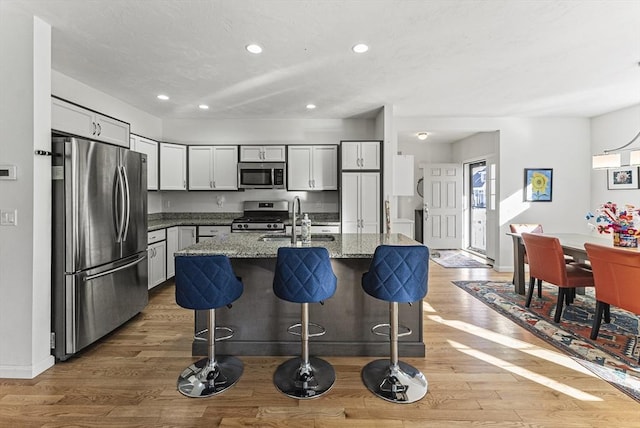 kitchen with wood-type flooring, stainless steel appliances, dark stone countertops, an island with sink, and sink