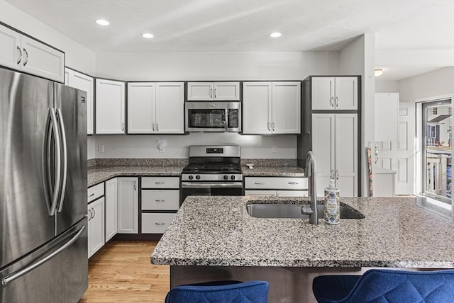 kitchen with light stone counters, sink, a center island with sink, and stainless steel appliances