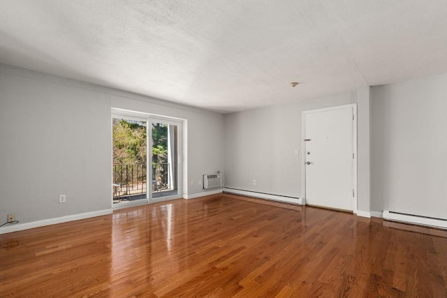 spare room featuring baseboards, a wall mounted air conditioner, wood finished floors, and baseboard heating