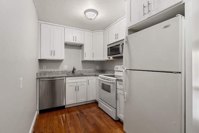 kitchen with white cabinets, light stone countertops, appliances with stainless steel finishes, a sink, and dark wood finished floors