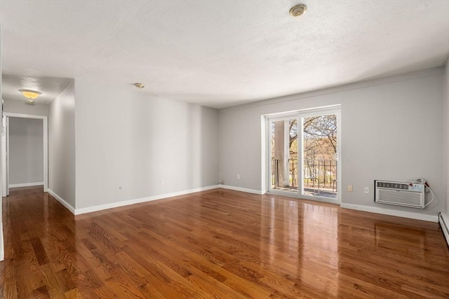spare room featuring baseboards, a wall mounted AC, and wood finished floors