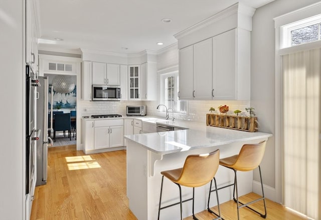 kitchen featuring a wealth of natural light, stainless steel microwave, light wood-style floors, and a peninsula