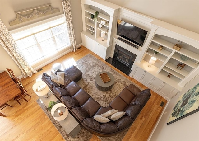 living area featuring baseboards, a fireplace with flush hearth, visible vents, and wood finished floors