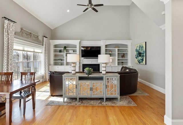 living area featuring baseboards, a fireplace, wood finished floors, high vaulted ceiling, and a ceiling fan