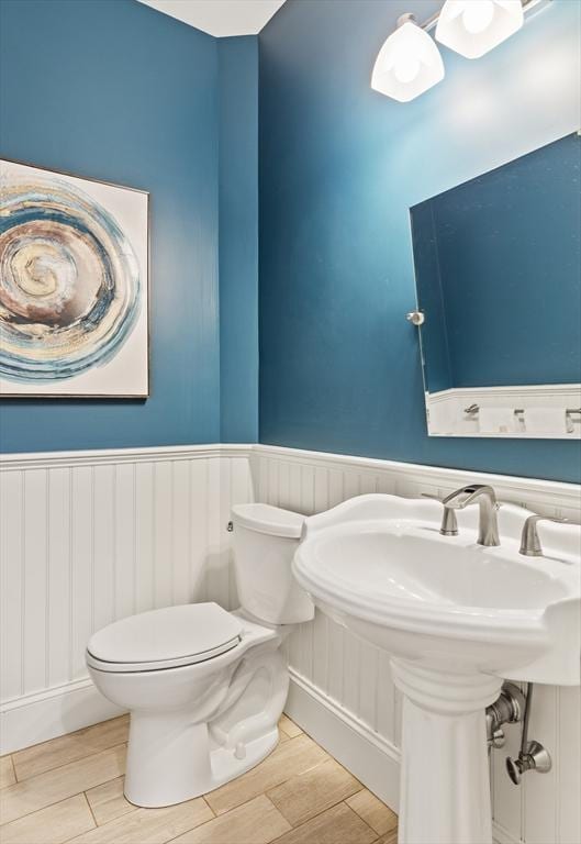 half bathroom featuring wainscoting, toilet, and wood finish floors