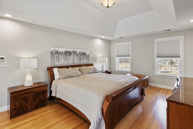 bedroom featuring a tray ceiling, light wood-type flooring, and baseboards