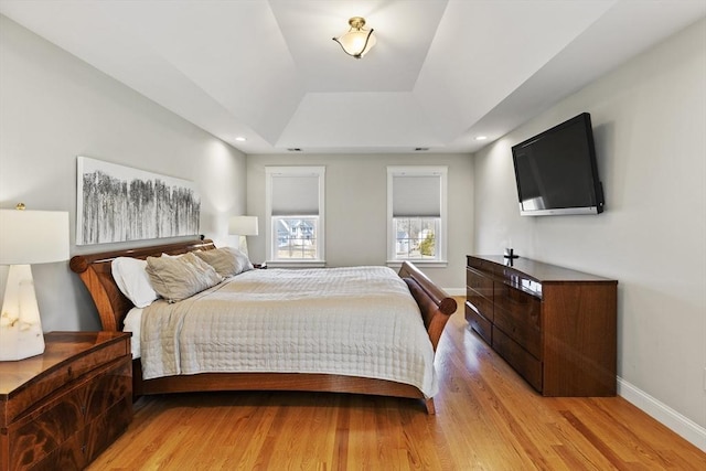 bedroom featuring a raised ceiling, recessed lighting, baseboards, and light wood finished floors