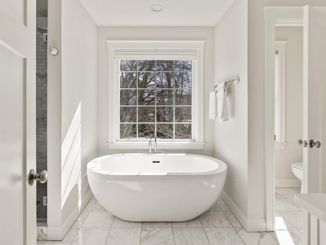 full bathroom with a freestanding bath, marble finish floor, toilet, and a healthy amount of sunlight