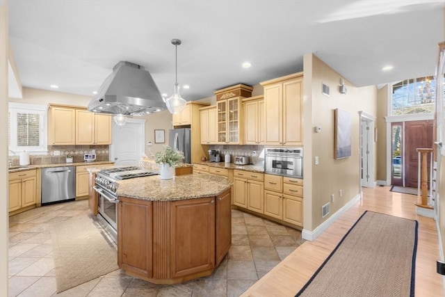 kitchen with island exhaust hood, tasteful backsplash, stainless steel appliances, a kitchen island, and hanging light fixtures