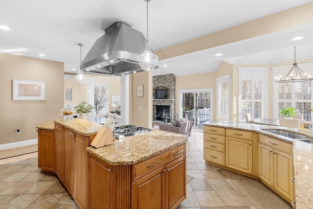 kitchen with light stone countertops, hanging light fixtures, a stone fireplace, island exhaust hood, and a kitchen island