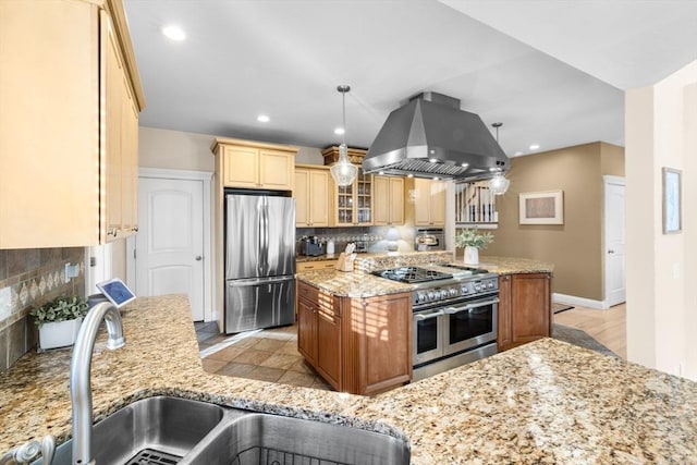 kitchen with sink, hanging light fixtures, light stone countertops, island range hood, and stainless steel appliances