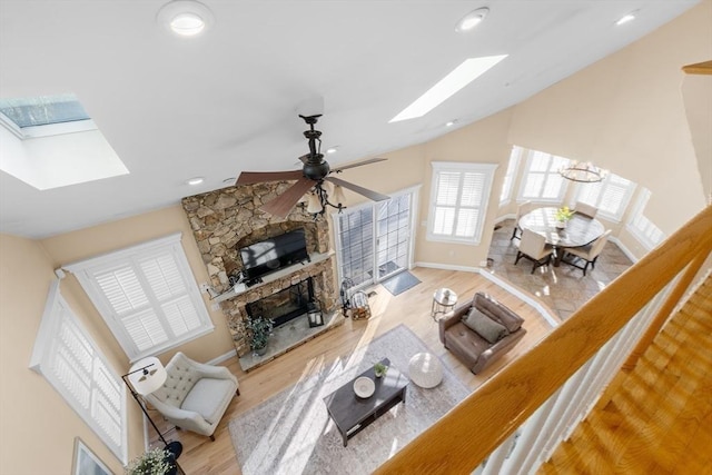 living room with a fireplace, vaulted ceiling with skylight, light hardwood / wood-style floors, and ceiling fan with notable chandelier