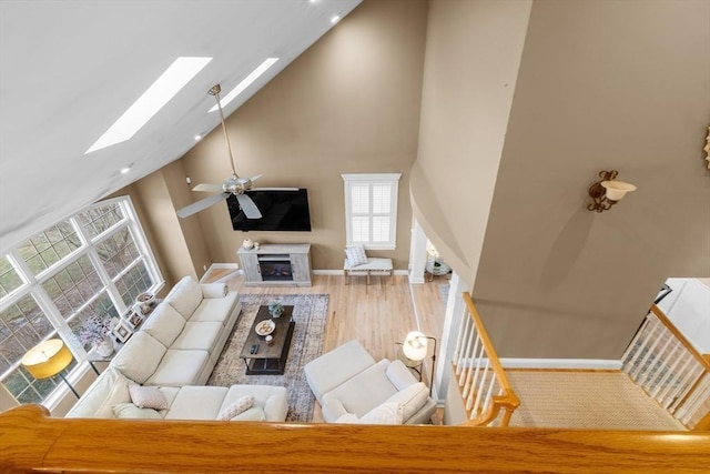 living room with hardwood / wood-style floors, ceiling fan, high vaulted ceiling, and a skylight