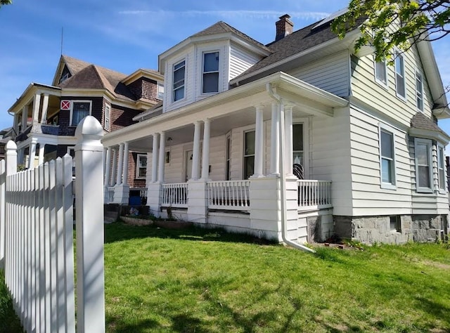 view of front of house with covered porch, a chimney, and a front lawn