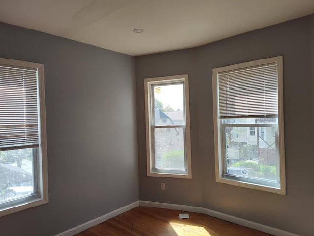 unfurnished room with a healthy amount of sunlight, baseboards, and wood finished floors