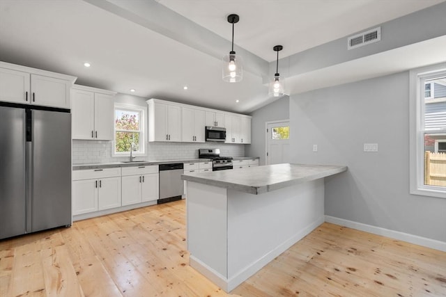kitchen with a sink, light wood finished floors, a peninsula, and stainless steel appliances