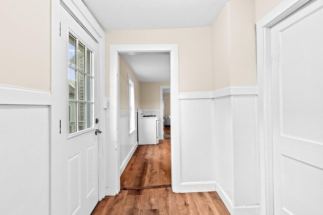 corridor featuring a wainscoted wall, washer / dryer, and wood finished floors