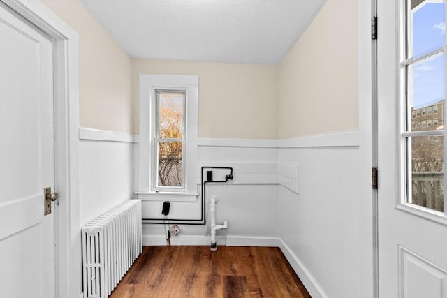 laundry area featuring radiator heating unit, wood finished floors, baseboards, and a healthy amount of sunlight