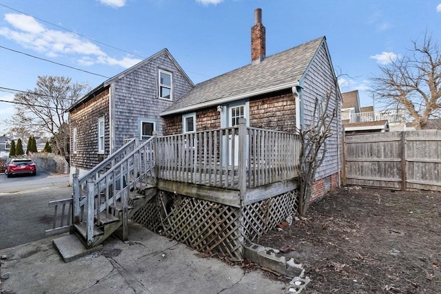 back of house featuring a wooden deck, a shingled roof, a chimney, and fence