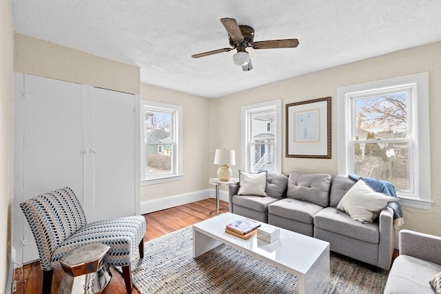 living room featuring ceiling fan, baseboards, a textured ceiling, and wood finished floors