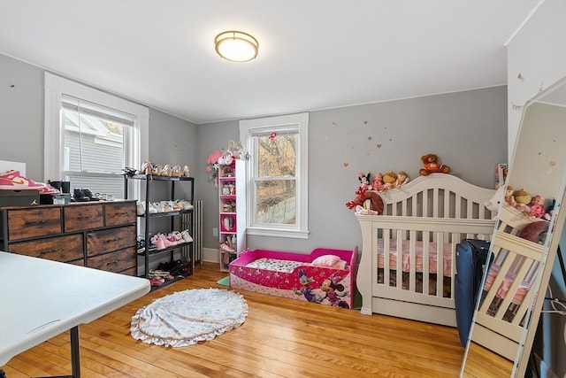 bedroom with multiple windows, a nursery area, and hardwood / wood-style flooring