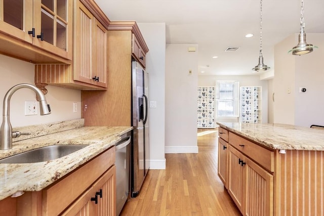 kitchen featuring sink, appliances with stainless steel finishes, hanging light fixtures, light hardwood / wood-style floors, and light stone countertops