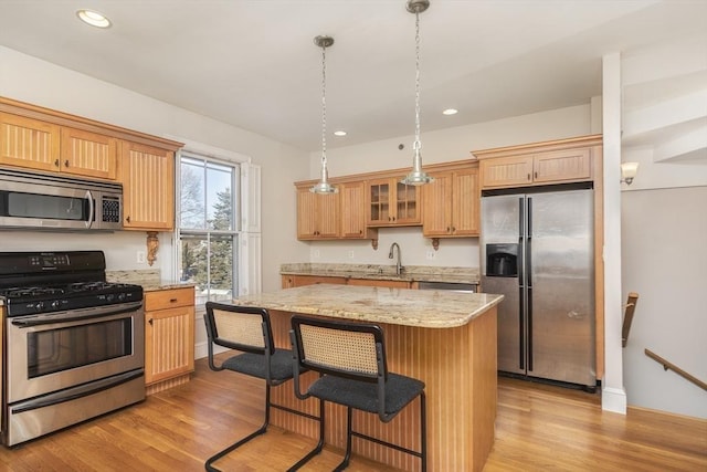 kitchen with a kitchen island, decorative light fixtures, light hardwood / wood-style floors, light stone counters, and stainless steel appliances