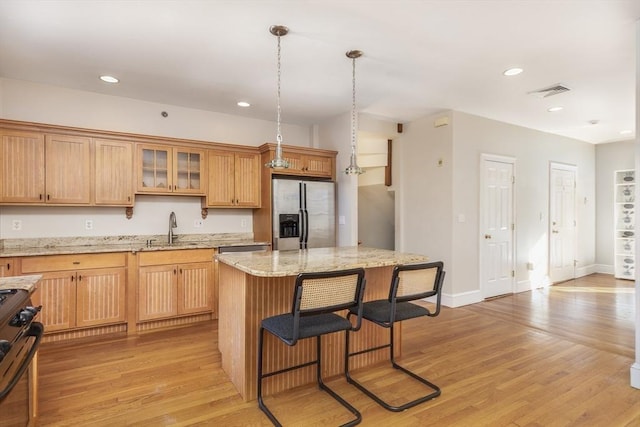 kitchen with sink, hanging light fixtures, stove, light stone counters, and stainless steel refrigerator with ice dispenser