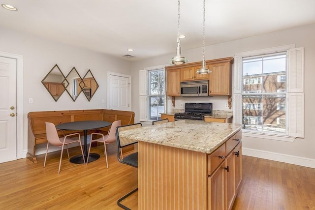 kitchen featuring black gas range oven, light stone counters, light hardwood / wood-style floors, a kitchen island, and decorative light fixtures