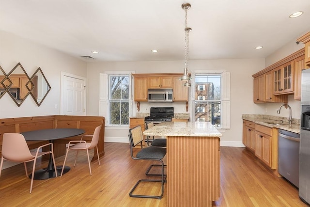 kitchen with stainless steel appliances, light stone counters, a kitchen island, decorative light fixtures, and light wood-type flooring