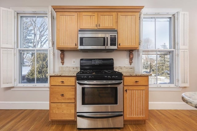 kitchen featuring stainless steel appliances, light stone countertops, light brown cabinets, and light wood-type flooring