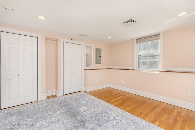 unfurnished bedroom with hardwood / wood-style floors, two closets, and electric panel