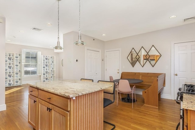 kitchen with light stone counters, light wood-type flooring, stainless steel range, a kitchen island, and pendant lighting