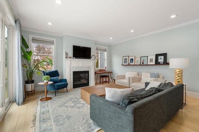 living area with crown molding, baseboards, light wood-type flooring, and a high end fireplace