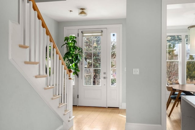 foyer entrance with a wealth of natural light, light wood-type flooring, and stairs