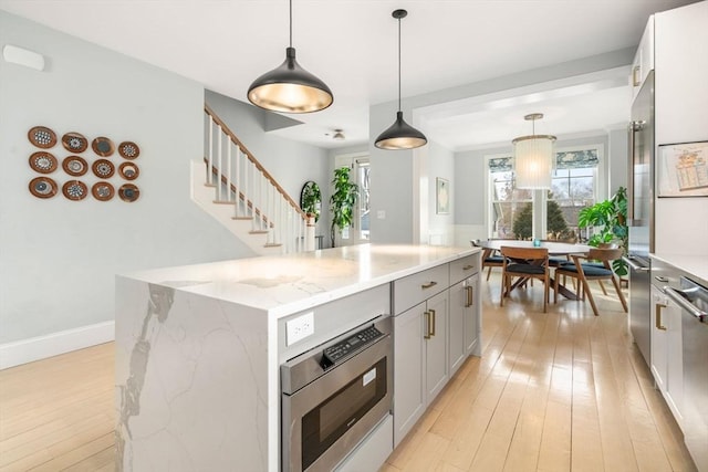 kitchen with a kitchen island, stainless steel appliances, light wood-type flooring, and light stone countertops