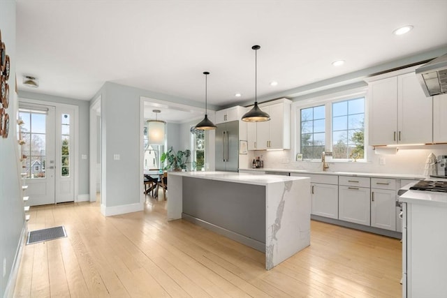 kitchen with decorative light fixtures, light wood-style flooring, a center island, and a sink