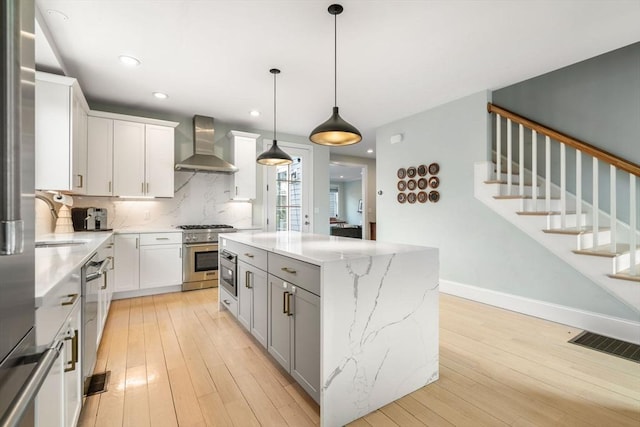 kitchen with wall chimney exhaust hood, light wood-style floors, visible vents, and stainless steel appliances