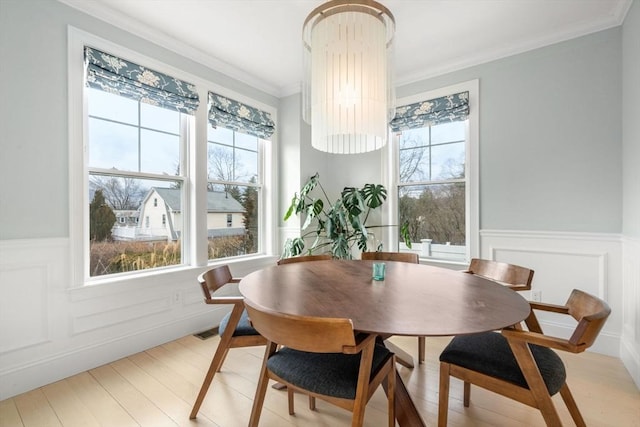 dining space featuring a wainscoted wall, visible vents, light wood-style floors, and ornamental molding