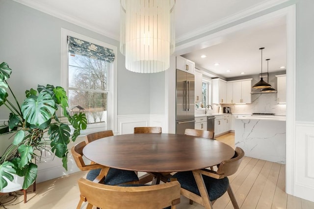 dining area with a decorative wall, light wood-style floors, wainscoting, and crown molding