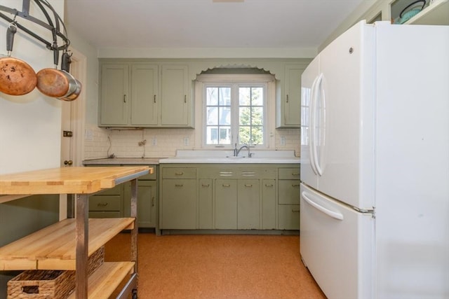 kitchen featuring freestanding refrigerator, green cabinetry, a sink, and tasteful backsplash