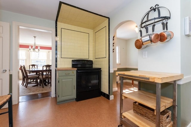kitchen featuring an inviting chandelier, arched walkways, baseboards, black / electric stove, and butcher block counters